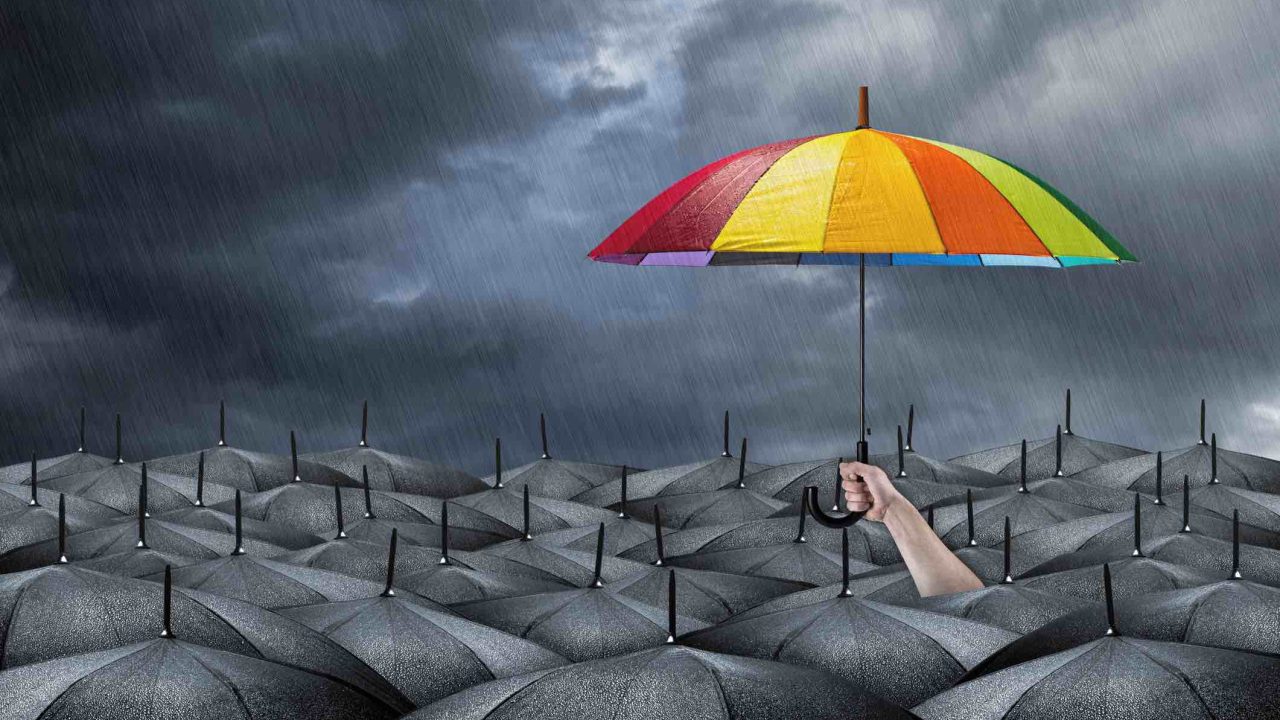 rainbow umbrella in mass of black umbrellas